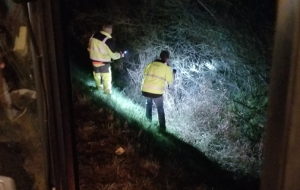 Zwei Straßenwärter mit Taschenlampen suchen in der Dunkelheit vergeblich nach einem verloren gegangenen Reifen.
