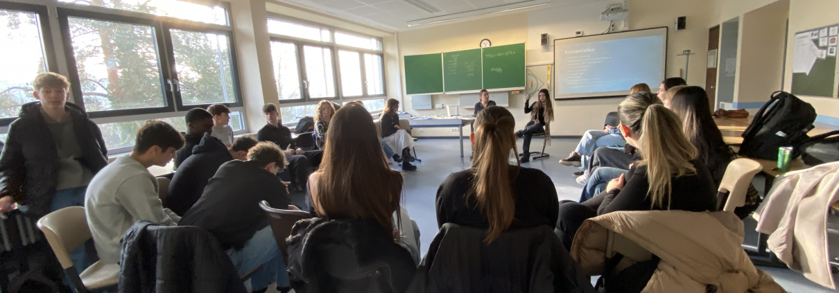 Klassenraum, Stuhlkreis, digitale Päsentation, vorne Moderatorin