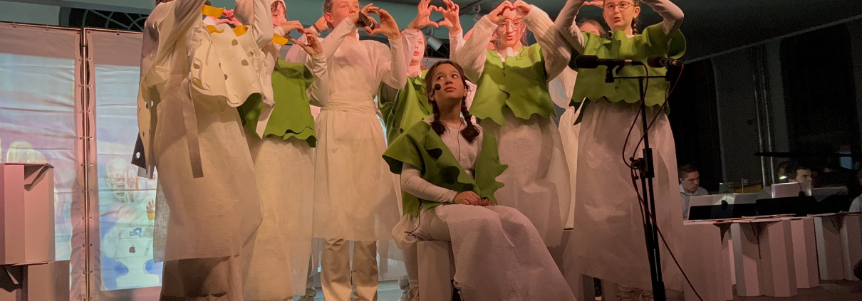 Bild aus Musical-Aufführung. Mädchen wird von Mitschülerinnen umringt.