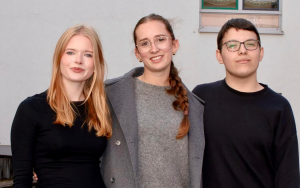 Zwei Schülerin und ein Schüler stehen nebeneinander und schauen erwartungsvoll