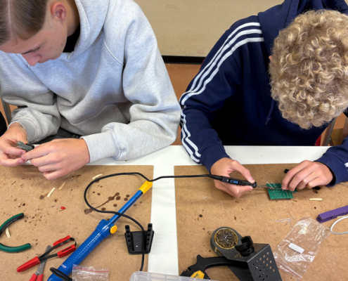 Zwei Jungen beugen sich über eine Platine und löten