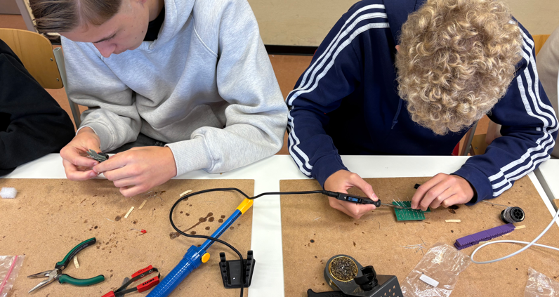Zwei Jungen beugen sich über eine Platine und löten