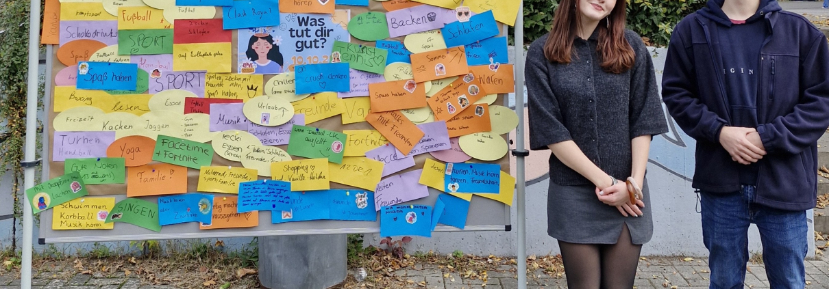 Das Schülersprecherteam steht neben einer Stellwand auf dem Schulhof.