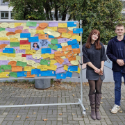 Das Schülersprecherteam steht neben einer Stellwand auf dem Schulhof.