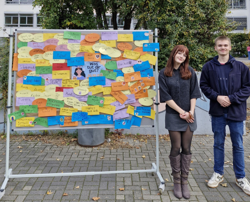 Das Schülersprecherteam steht neben einer Stellwand auf dem Schulhof.