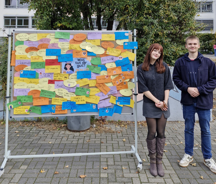 Das Schülersprecherteam steht neben einer Stellwand auf dem Schulhof.