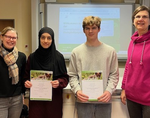 2 Schüler mit Urkunde in einem Klassenraum, rechts und links von ihnen die Fachlehrerin und die Schulleiterin.