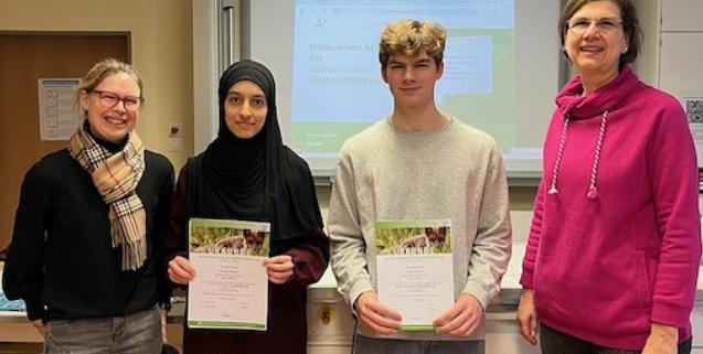 2 Schüler mit Urkunde in einem Klassenraum, rechts und links von ihnen die Fachlehrerin und die Schulleiterin.