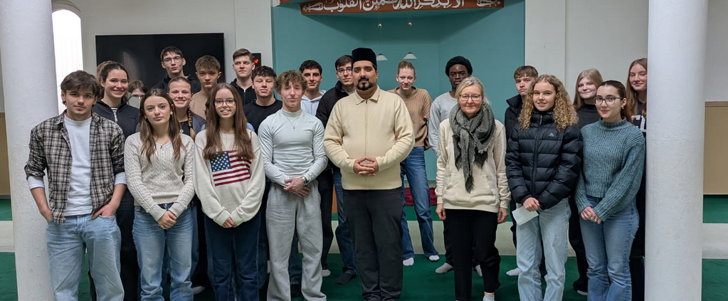 Schülergruppe steht mit Iman in der Moschee vor der Gebetsnische