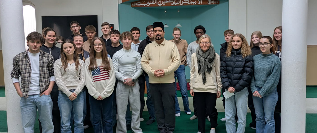 Schülergruppe steht mit Iman in der Moschee vor der Gebetsnische