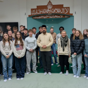 Schülergruppe steht mit Iman in der Moschee vor der Gebetsnische