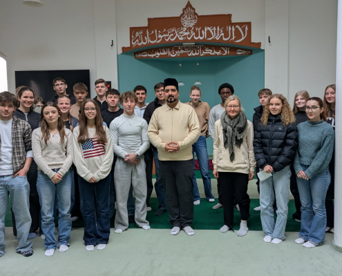 Schülergruppe steht mit Iman in der Moschee vor der Gebetsnische