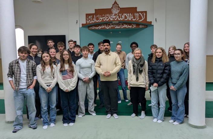 Schülergruppe steht mit Iman in der Moschee vor der Gebetsnische
