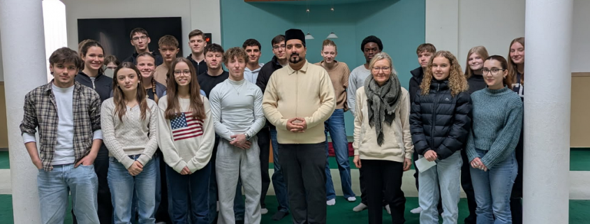 Schülergruppe steht mit Iman in der Moschee vor der Gebetsnische