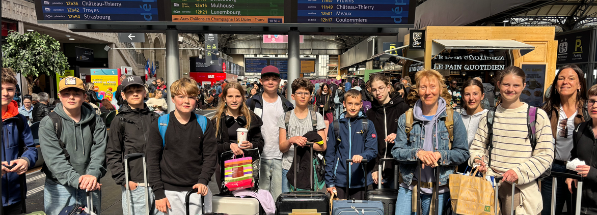 eine Gruppe von 15 Schülerinnen und Schülern mit Gepäck wartet in einem französischem Bahnhof