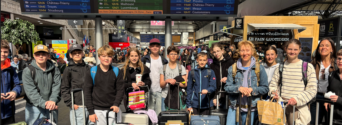 eine Gruppe von 15 Schülerinnen und Schülern mit Gepäck wartet in einem französischem Bahnhof
