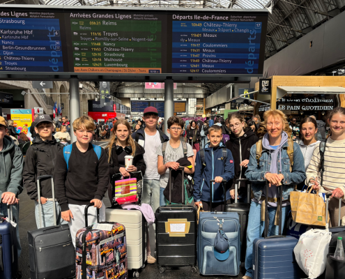 eine Gruppe von 15 Schülerinnen und Schülern mit Gepäck wartet in einem französischem Bahnhof